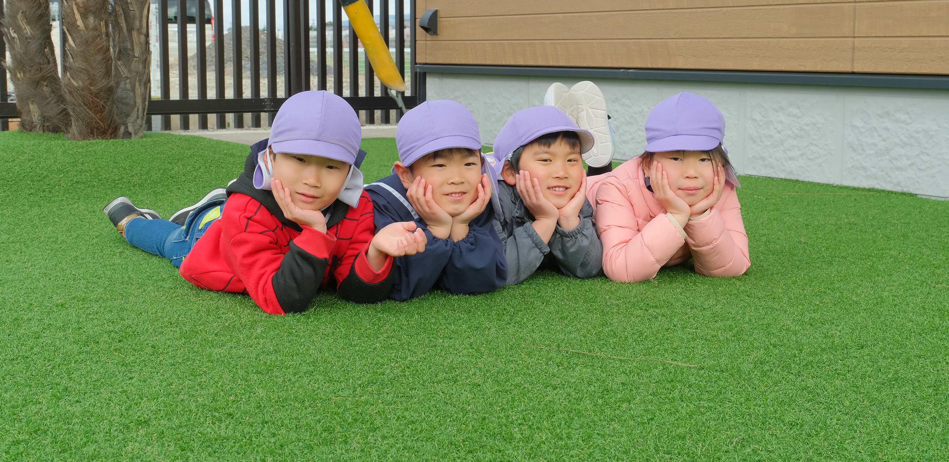 4人の4歳児が並んで寝転んで肘をついてこちらを向いている様子